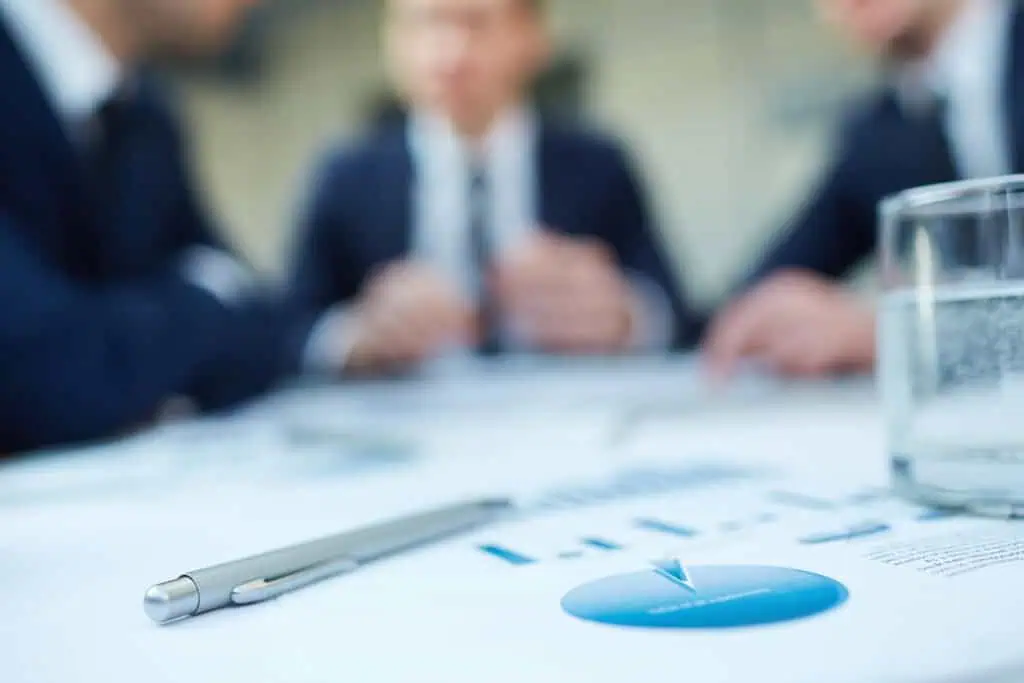 Image of business document and pen at workplace with group of colleagues interacting in background