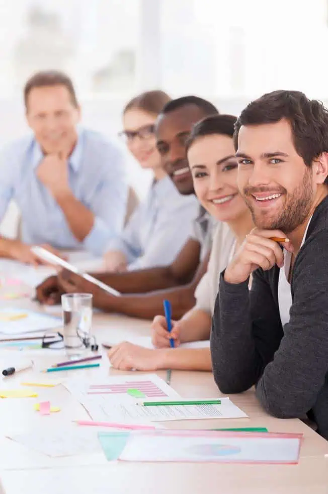Group of business people in meeting room wearing casual wear sitting in a row at the table and smiling